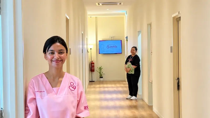 Avida caregiver in the centre’s pink uniform, with a colleague in the corridor; retouched photograph